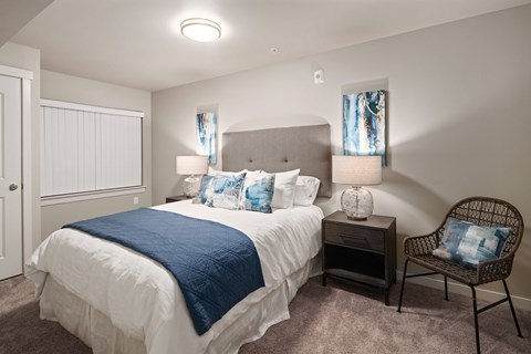 A bedroom with a bed, chair, and nightstand.