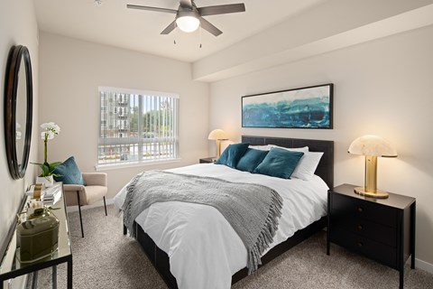 A bedroom with a large bed, a ceiling fan, and a painting on the wall.