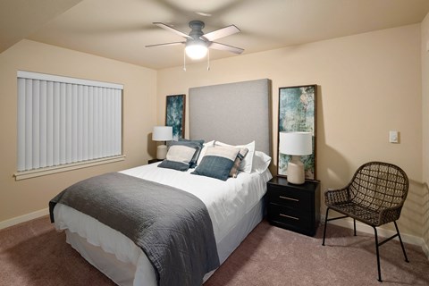 A bedroom with a bed, chair, and ceiling fan.