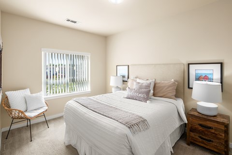 A bedroom with a bed, chair, and two lamps.