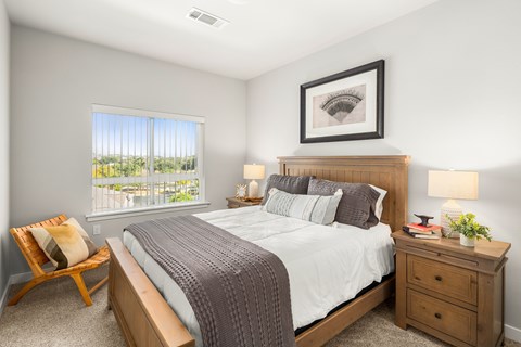 A bedroom with a large bed, a chair, and a window overlooking a balcony.