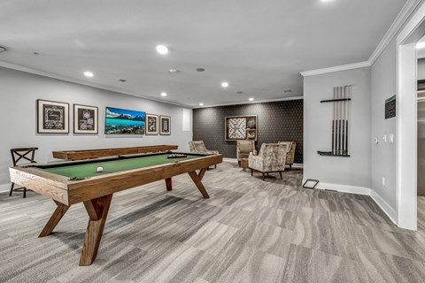 A pool table is in the middle of a room with a chair and pictures on the wall.