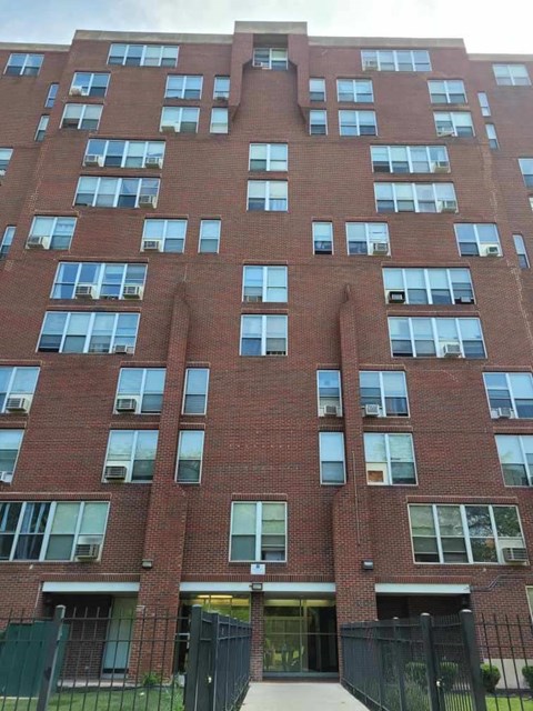A tall red brick building with many windows and a black fence in front.