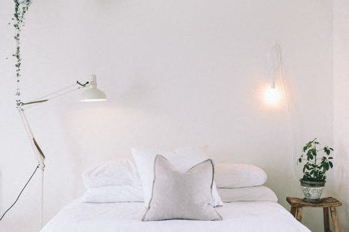 A white bed with a white pillow and a white lamp.