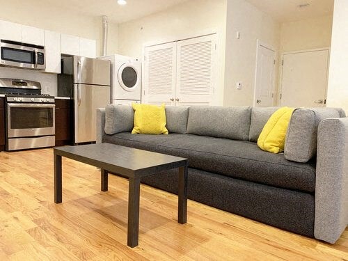 A grey couch with yellow pillows sits in a kitchen with a wooden floor.