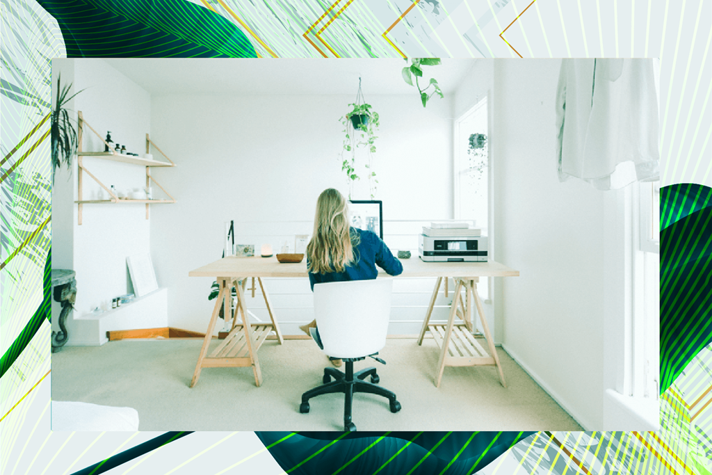 A woman is sitting at a desk in a room with a laptop and a plant.