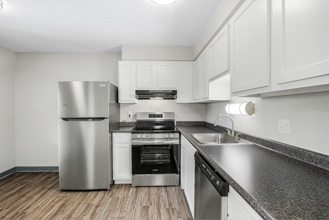A modern kitchen with a stainless steel refrigerator and black countertops.