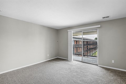 A room with a carpeted floor and a sliding glass door leading to a balcony.