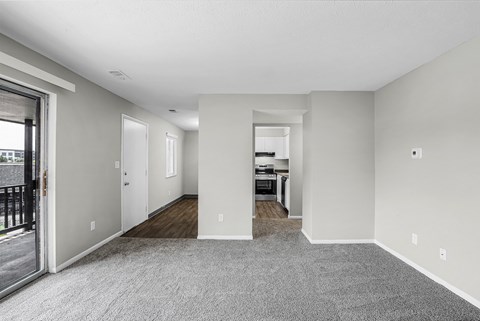 A spacious living room with a grey carpet and white walls.