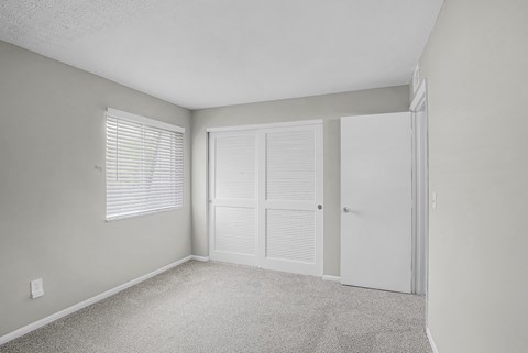 A room with a carpeted floor, two doors, and a window with blinds.
