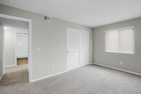 A room with a carpeted floor and a window with blinds.