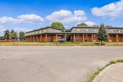 A large, empty parking lot in front of a brick building with a green tree in front of it.