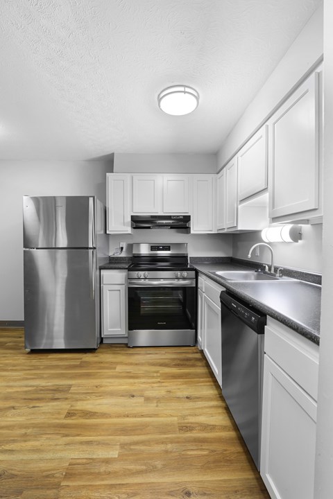 A modern kitchen with a stainless steel refrigerator, oven, and wooden flooring.