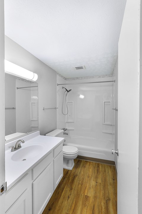 A white bathroom with wooden floors and a toilet.