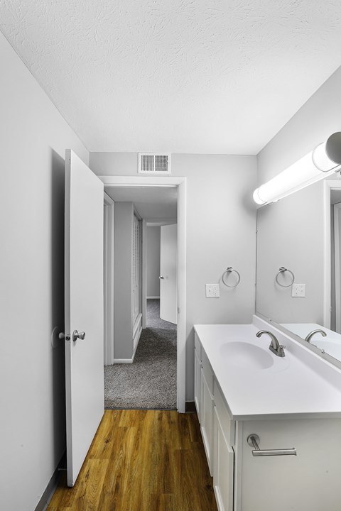 A white bathroom with a sink, mirror, and wooden floor.