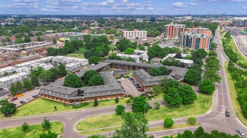 A large building with a green roof is surrounded by trees and other buildings.