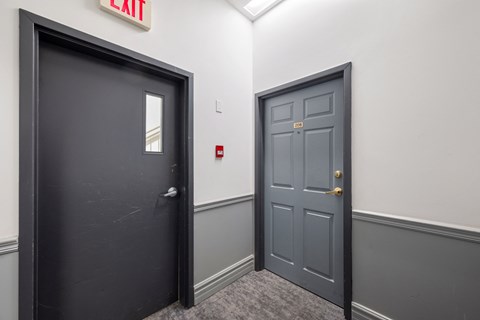 a hallway with two doors and a red fire alarm on the wall