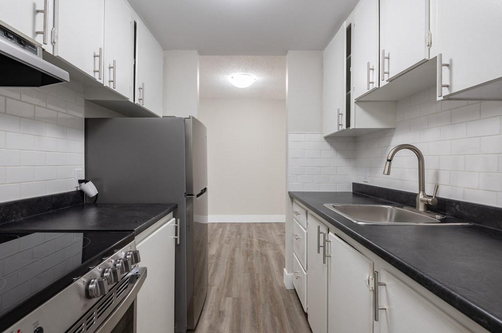 a kitchen with black counter tops and white cabinets and a stainless steel refrigerator