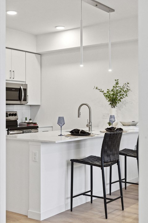 a kitchen with white cabinets and a white island with two black chairs
