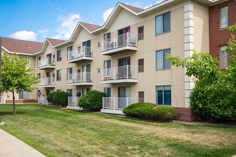an exterior view of an apartment building with a lawn and trees