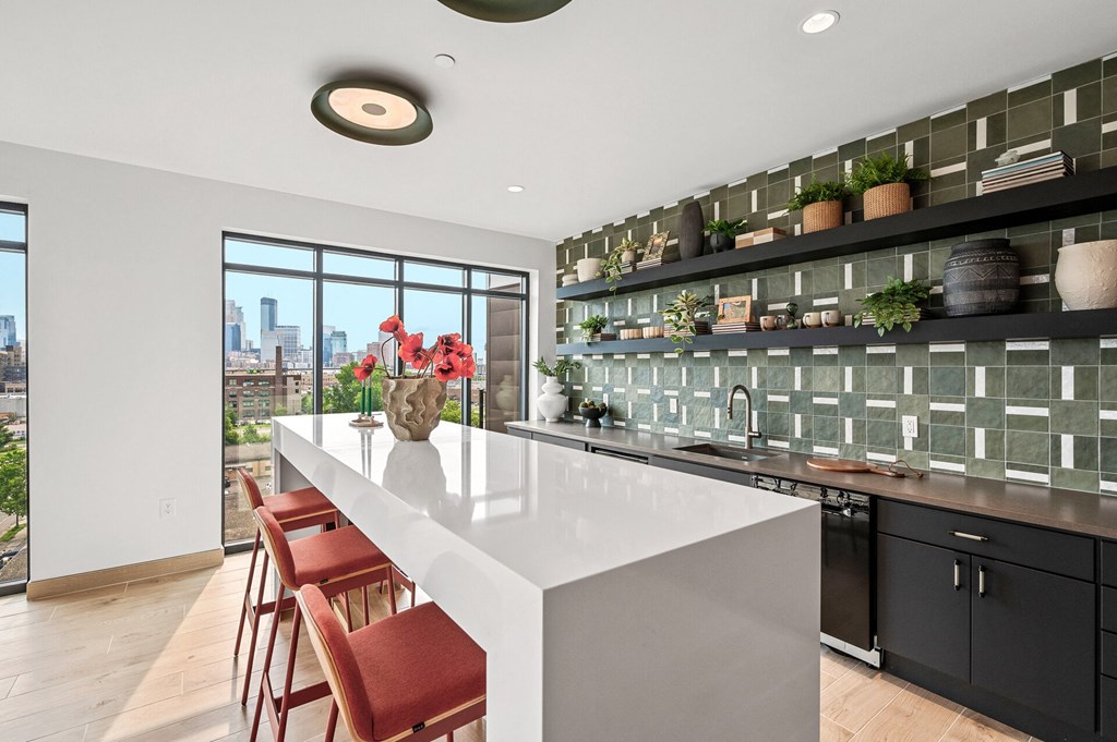 Community rooom kitchen with a white counter top and a large island with red chairs