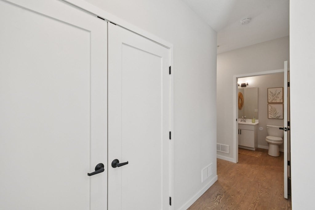 A white bathroom with a toilet and sink and hallway storage  at Ironwood Townhomes in Medina, Minnesota.