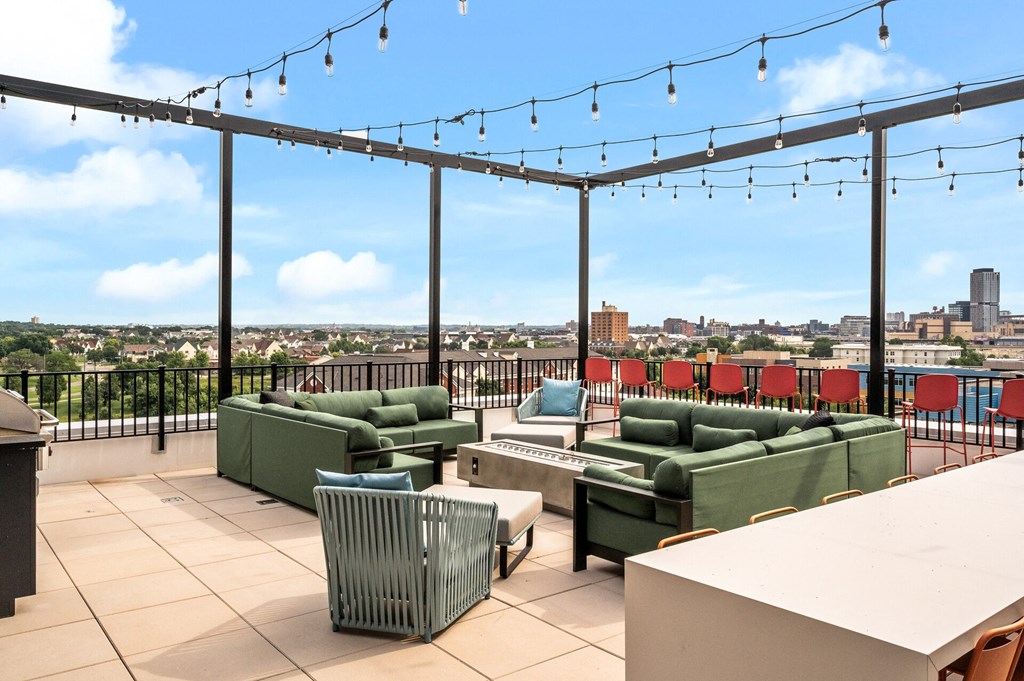 a rooftop patio with green couches and chairs and a view of the city