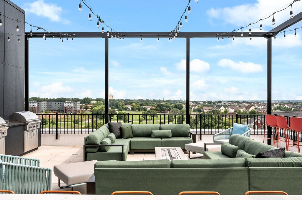Rooftop deck with green couches and a view of a city from a balcony