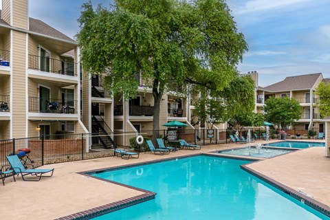 A swimming pool surrounded by chairs and trees in a residential area.