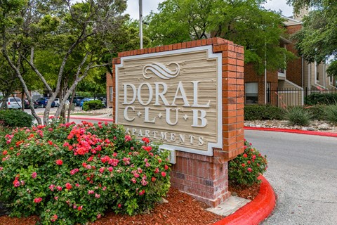 A sign for Doral Club Apartments is surrounded by flowers and greenery.