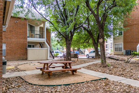 A picnic table sits in the middle of a gravel area between two apartment buildings.