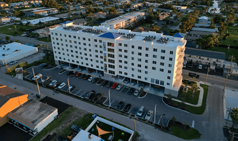 A large white hotel with a parking lot in front.