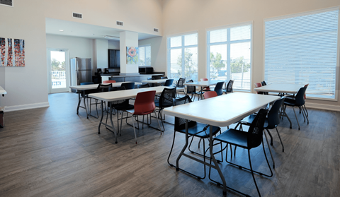 A room with tables and chairs and a fridge in the corner.