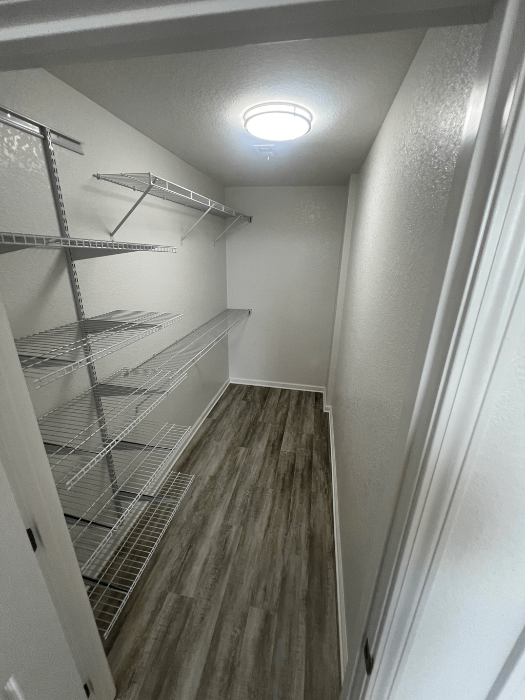 A long, narrow walk-in closet with shelving and a light on the ceiling.