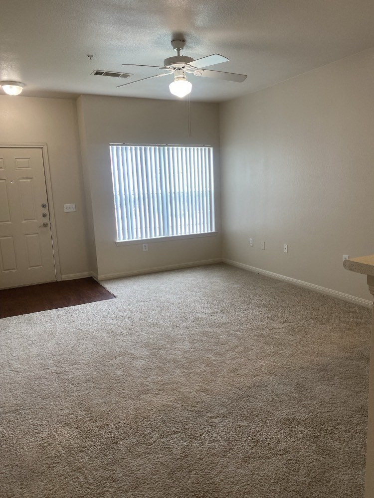 an empty living room with a window and a ceiling fan