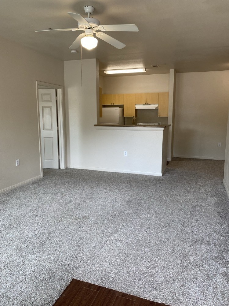an empty living room with a ceiling fan and a kitchen