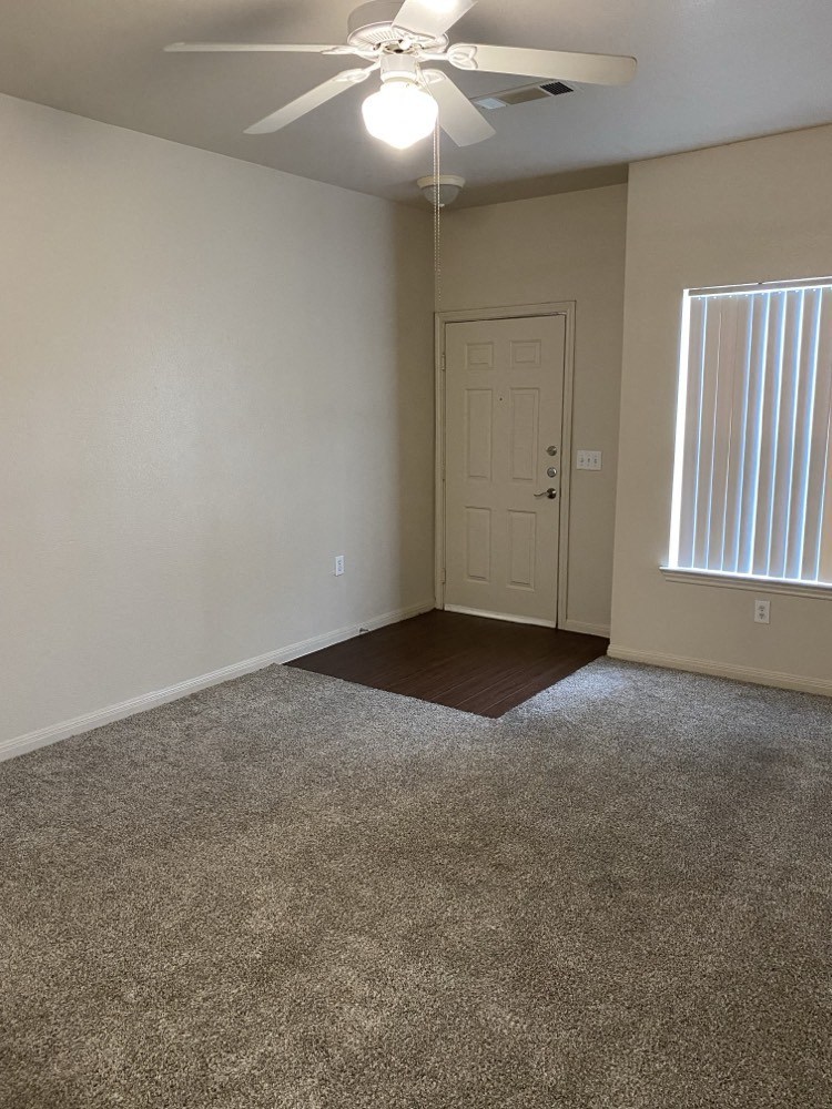 an empty living room with a ceiling fan and a window