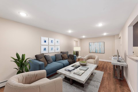 A living room with a blue couch, a grey coffee table, a beige armchair, and a painting on the wall.