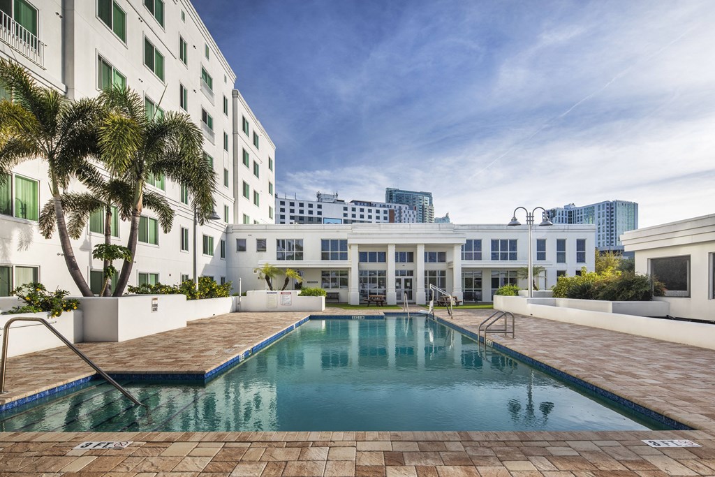 a swimming pool in front of a white building with palm trees