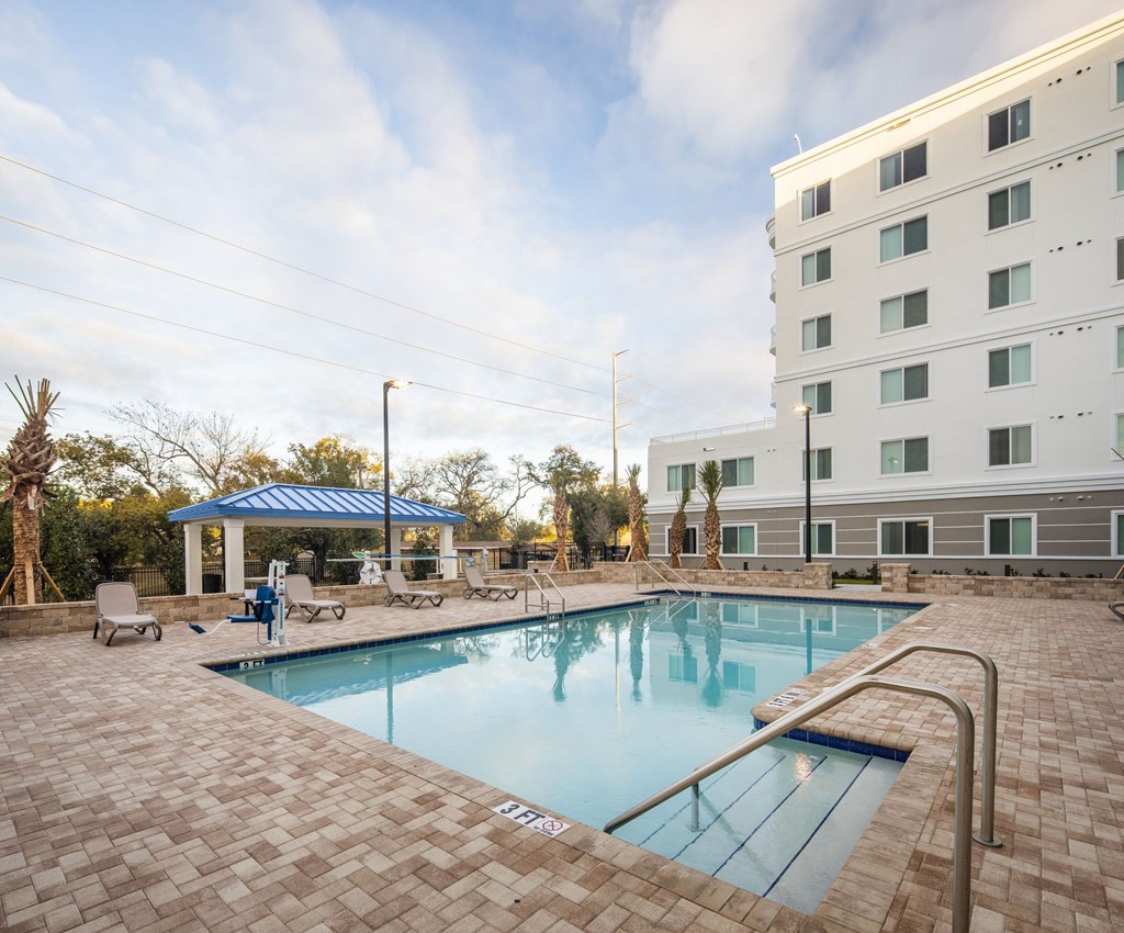 A swimming pool surrounded by a brick patio and a white building in the background.