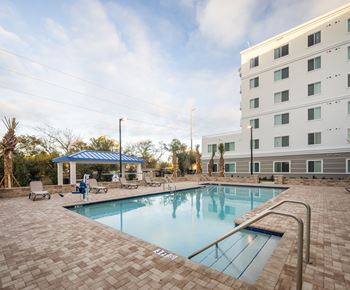 A swimming pool surrounded by a brick patio and a white building in the background.