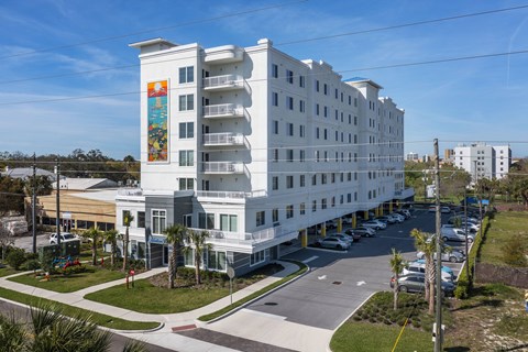 an aerial view of a white hotel building with palm trees and a parking lot