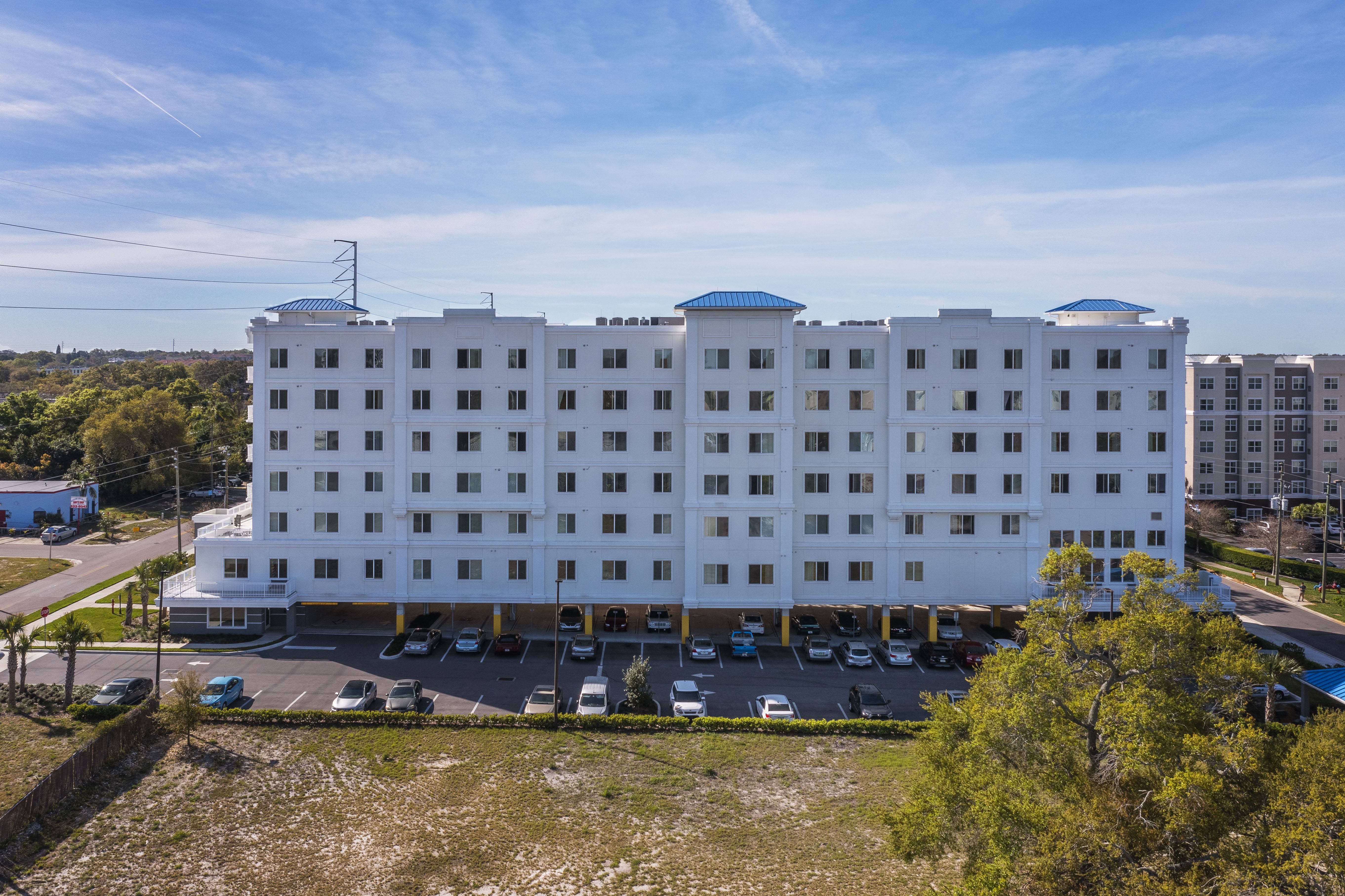 the facade of a white hotel with cars parked in a parking lot