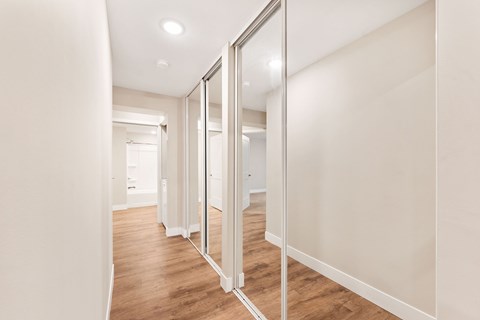 A hallway with a mirrored closet space with lots of storage and wooden floors.
