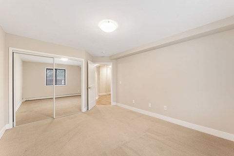 Spacious, unfurnished bedroom with large window, neutral walls, and plush carpeting in a modern apartment unit.