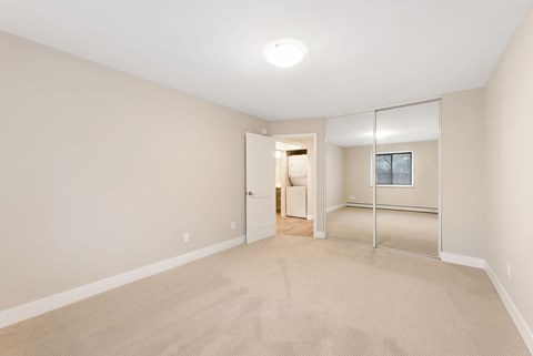 Large room with a carpeted floor and a mirrored doorway leading to another room.