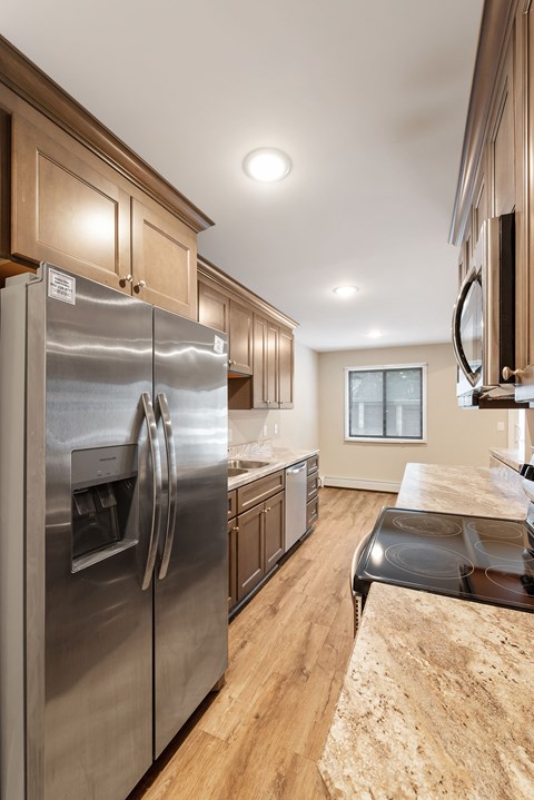 A modern kitchen with a stainless steel refrigerator and wooden cabinets. Santa Vera Apartments in Chanhassen, Minnesota