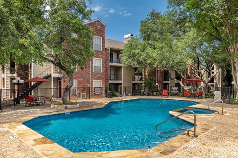 A swimming pool surrounded by trees and a building in the background.