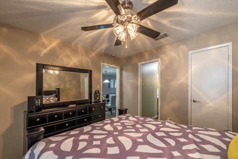 A bedroom with a bed, dresser, mirror, and ceiling fan.