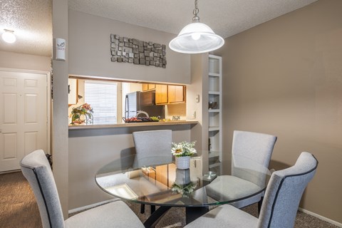 A dining room with a glass table and grey chairs.